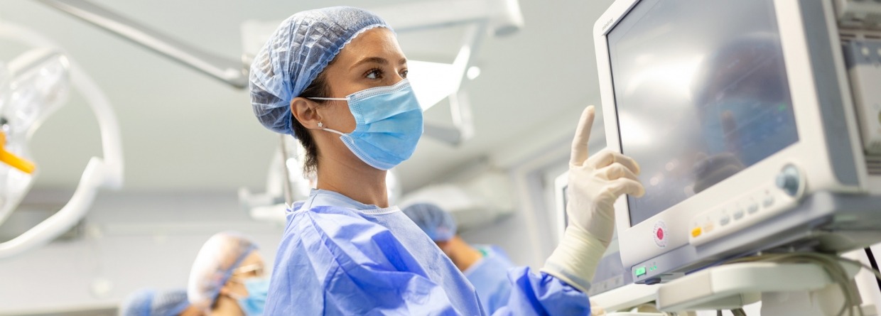 Jonge vrouwelijke arts in operatiekleding en een beschermend gezichtsmasker dat een anesthesiemachine voorbereidt voor een operatie
